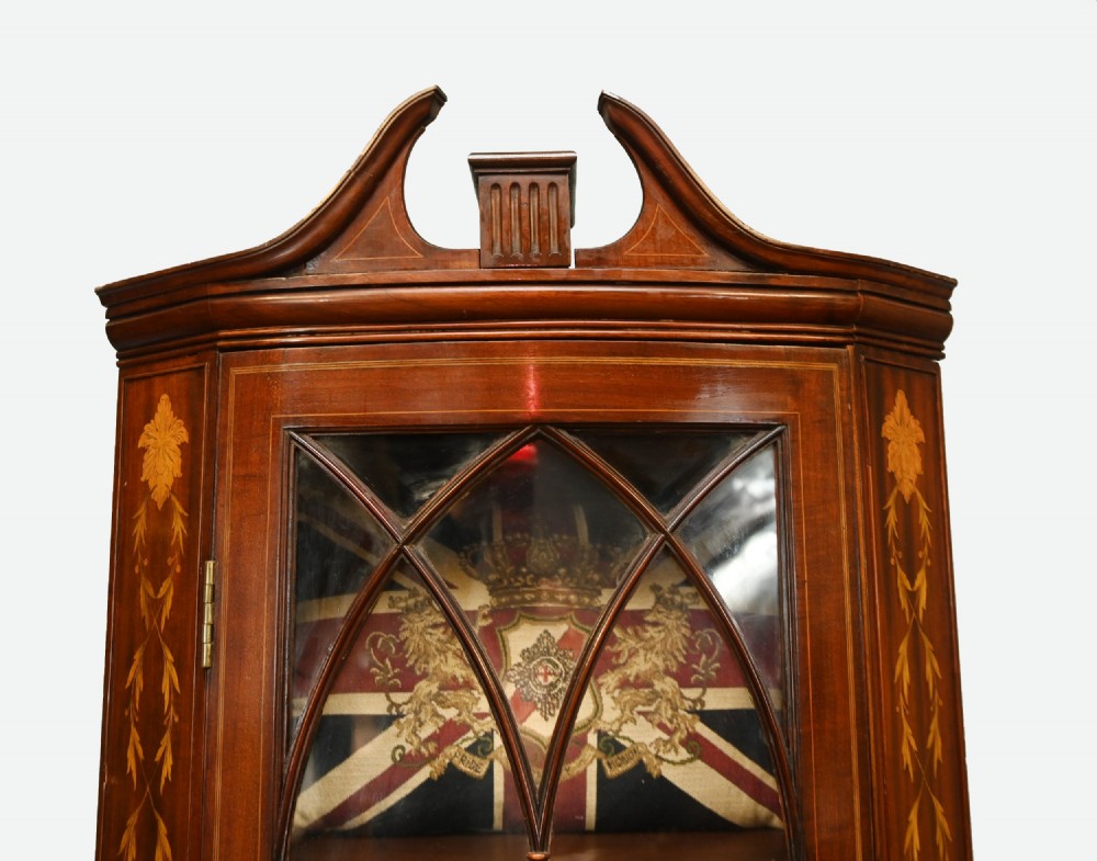 An Edwardian inlaid mahogany corner display cabinet featuring a swan-neck pediment, astragal glazed upper door, and marquetry urn designs on the lower panel. View IV