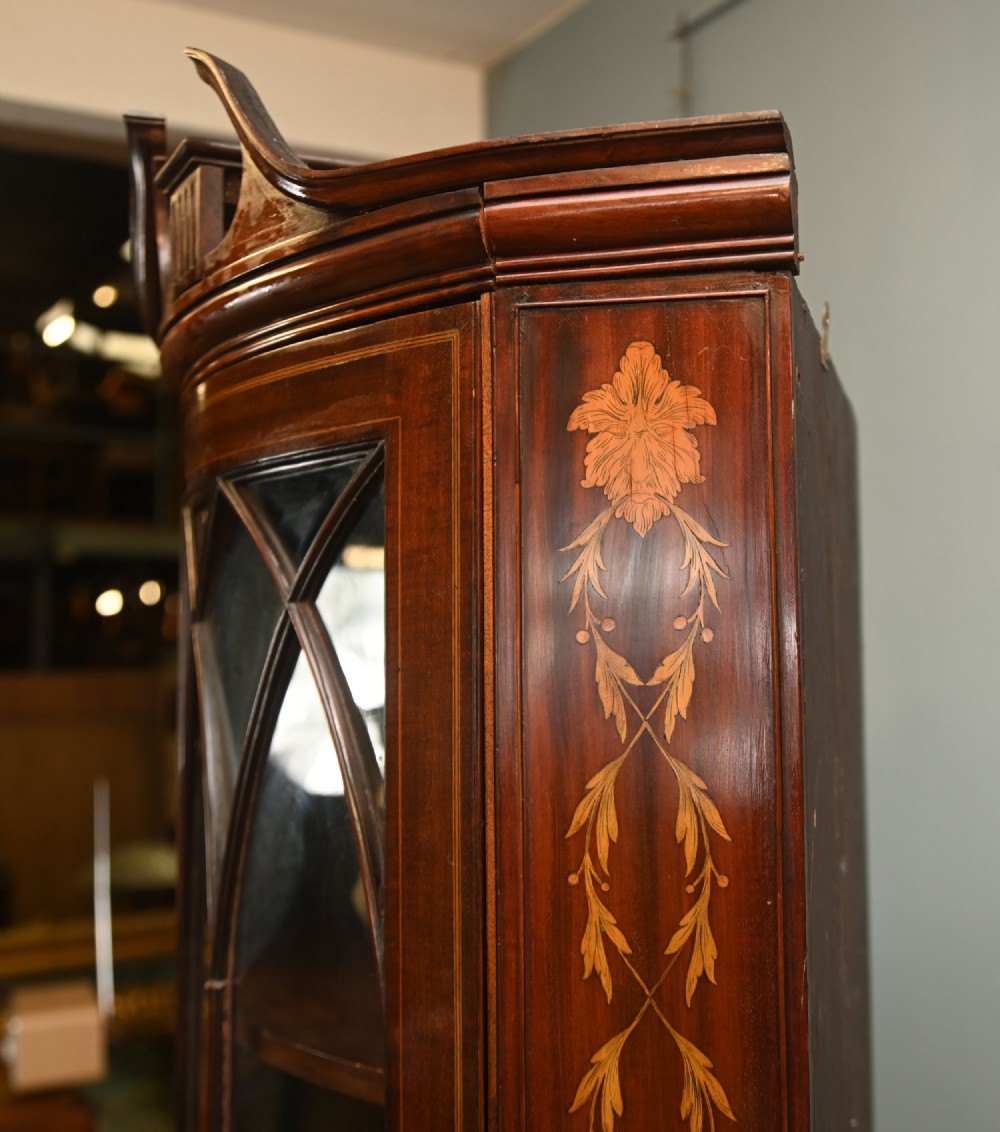 An Edwardian inlaid mahogany corner display cabinet featuring a swan-neck pediment, astragal glazed upper door, and marquetry urn designs on the lower panel. View V