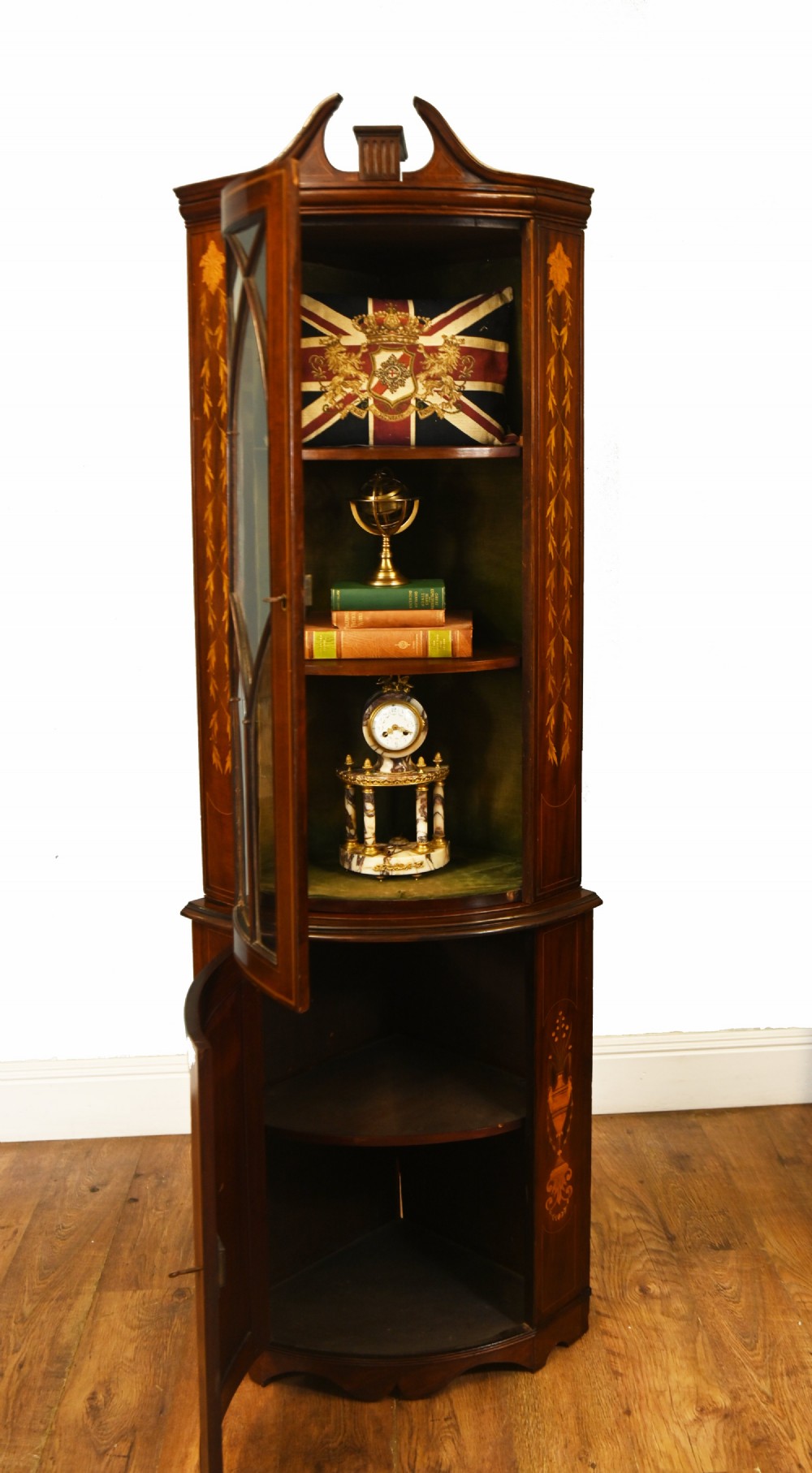 An Edwardian inlaid mahogany corner display cabinet featuring a swan-neck pediment, astragal glazed upper door, and marquetry urn designs on the lower panel. View VII