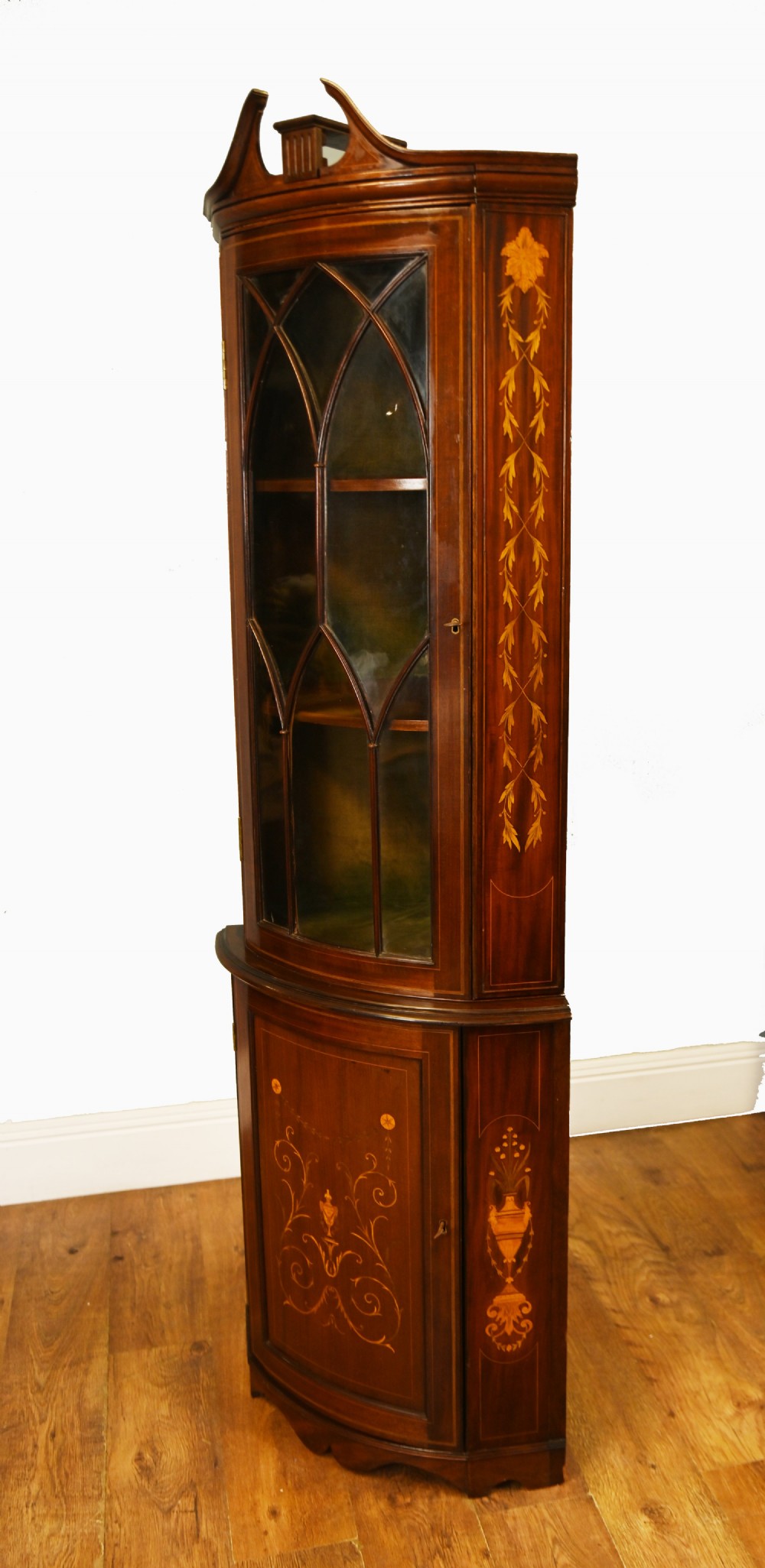 An Edwardian inlaid mahogany corner display cabinet featuring a swan-neck pediment, astragal glazed upper door, and marquetry urn designs on the lower panel. View VIII