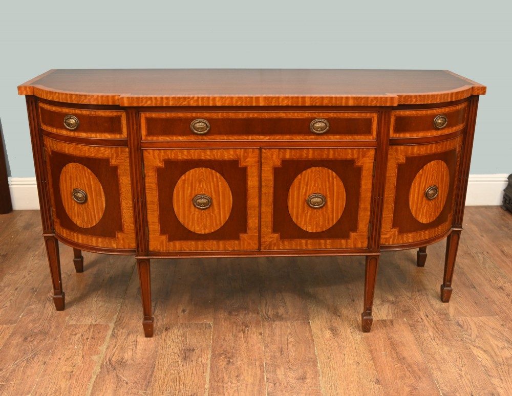 An Edwardian Sheraton Revival mahogany sideboard featuring satinwood oval inlay panels, crossbanded edging, brass ring handles, and square tapered legs.