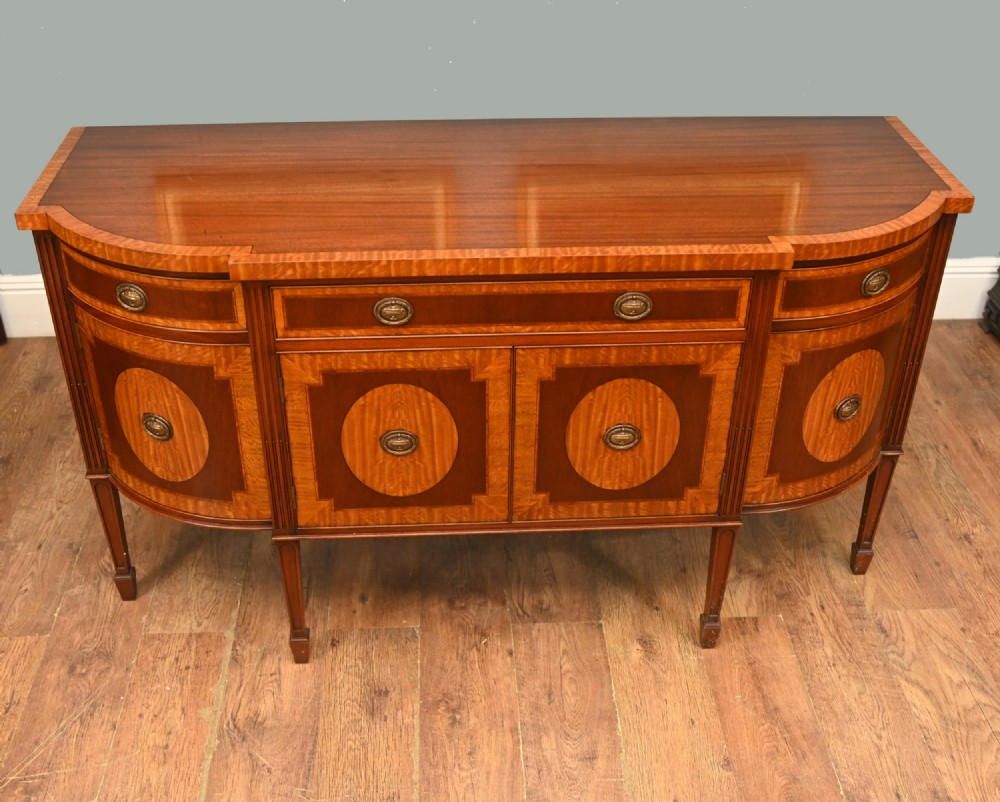 An Edwardian Sheraton Revival mahogany sideboard featuring satinwood oval inlay panels, crossbanded edging, brass ring handles, and square tapered legs. View IV