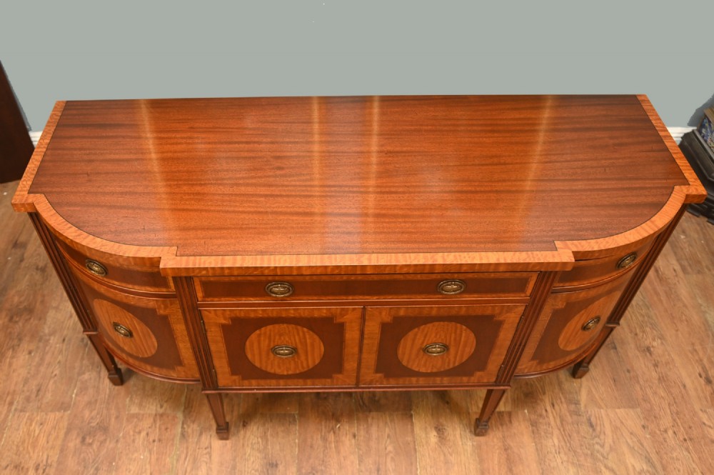An Edwardian Sheraton Revival mahogany sideboard featuring satinwood oval inlay panels, crossbanded edging, brass ring handles, and square tapered legs. View V