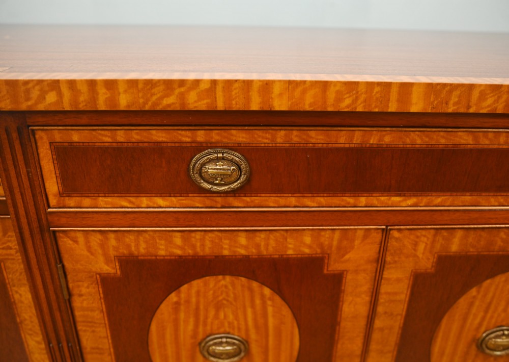 An Edwardian Sheraton Revival mahogany sideboard featuring satinwood oval inlay panels, crossbanded edging, brass ring handles, and square tapered legs. View VI