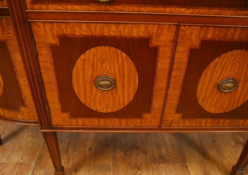 An Edwardian Sheraton Revival mahogany sideboard featuring satinwood oval inlay panels, crossbanded edging, brass ring handles, and square tapered legs. View VII