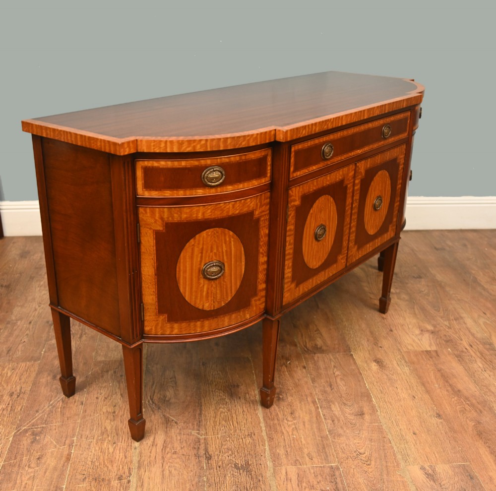An Edwardian Sheraton Revival mahogany sideboard featuring satinwood oval inlay panels, crossbanded edging, brass ring handles, and square tapered legs. View VIII