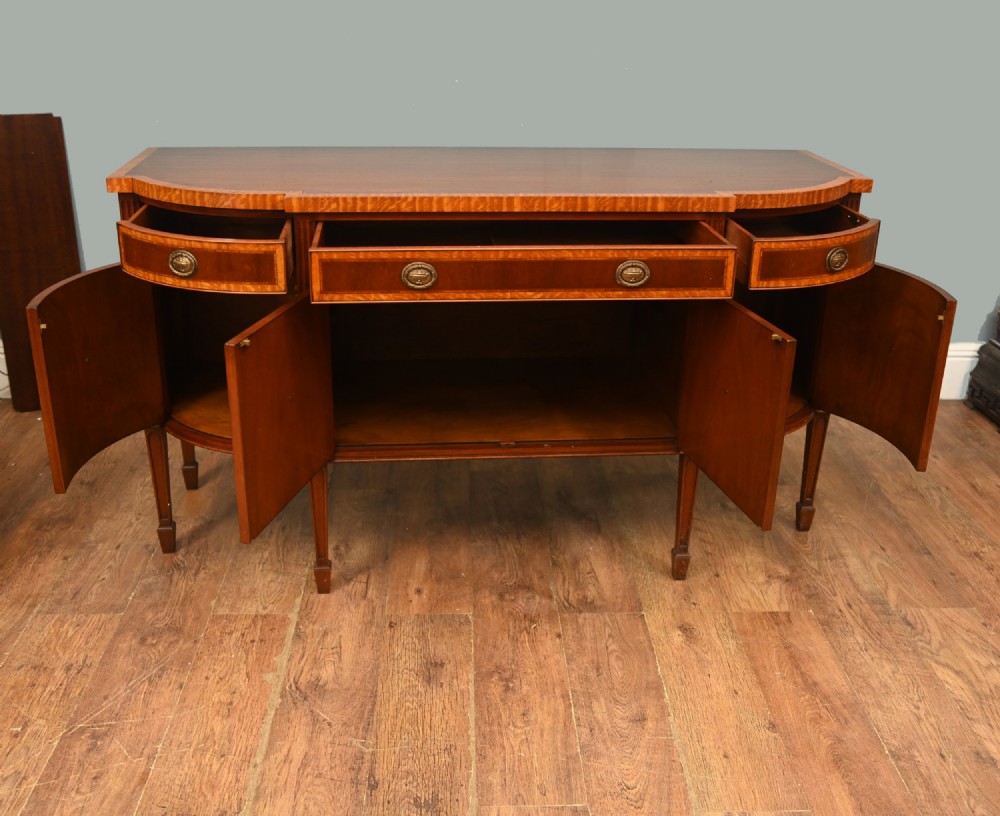 An Edwardian Sheraton Revival mahogany sideboard featuring satinwood oval inlay panels, crossbanded edging, brass ring handles, and square tapered legs. View IX