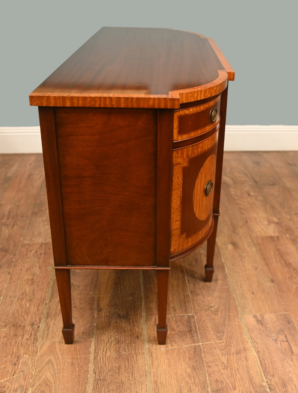 An Edwardian Sheraton Revival mahogany sideboard featuring satinwood oval inlay panels, crossbanded edging, brass ring handles, and square tapered legs. View XI