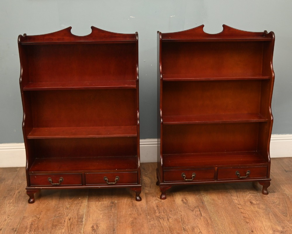 A pair of open mahogany waterfall bookcases featuring three graduated shelves, shaped side profiles, and two lower drawers.