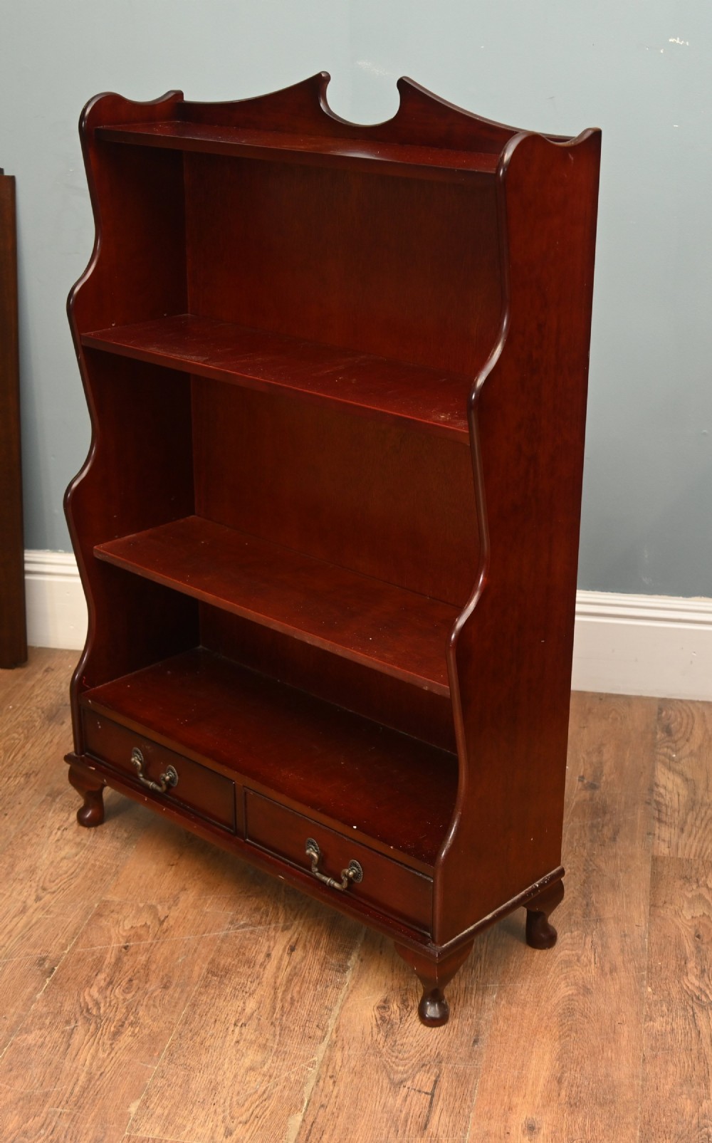 A pair of open mahogany waterfall bookcases featuring three graduated shelves, shaped side profiles, and two lower drawers. View VII