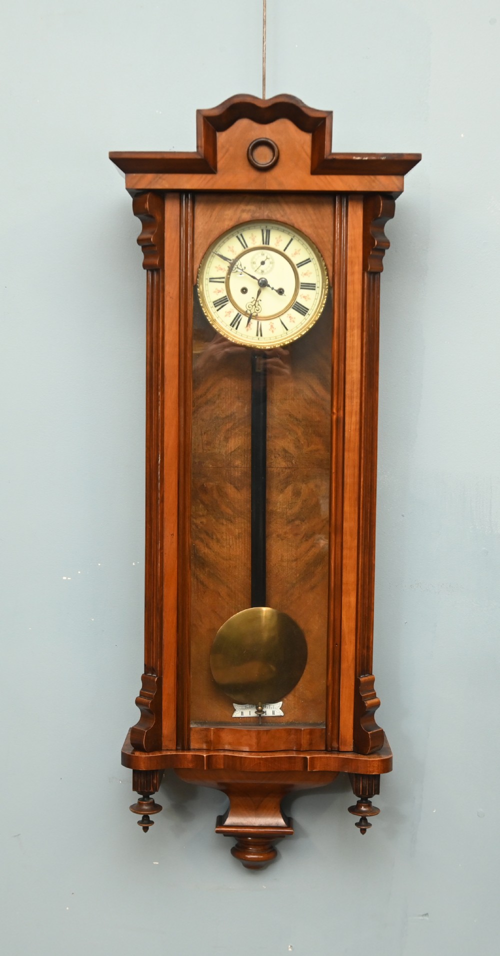 An antique walnut Vienna regulator wall clock featuring a glazed front door, brass pendulum, and turned bottom finials.