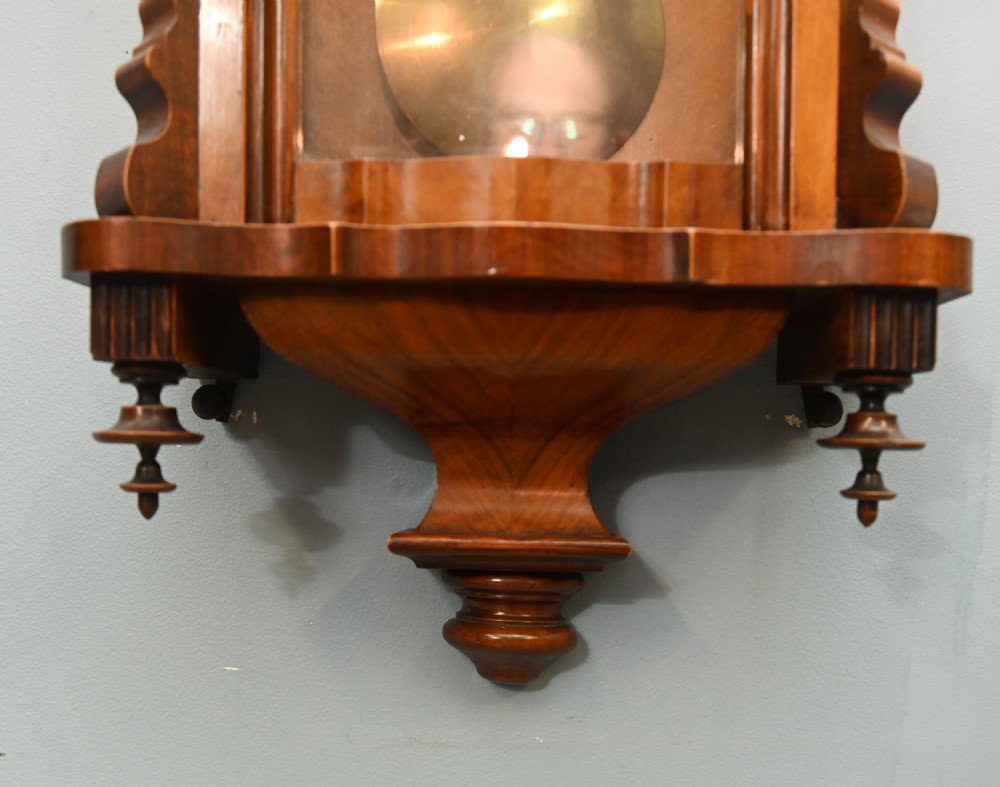 An antique walnut Vienna regulator wall clock featuring a glazed front door, brass pendulum, and turned bottom finials. View IV