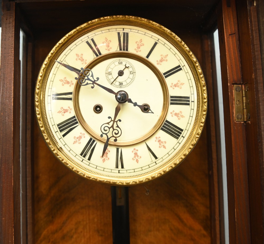 An antique walnut Vienna regulator wall clock featuring a glazed front door, brass pendulum, and turned bottom finials. View VI
