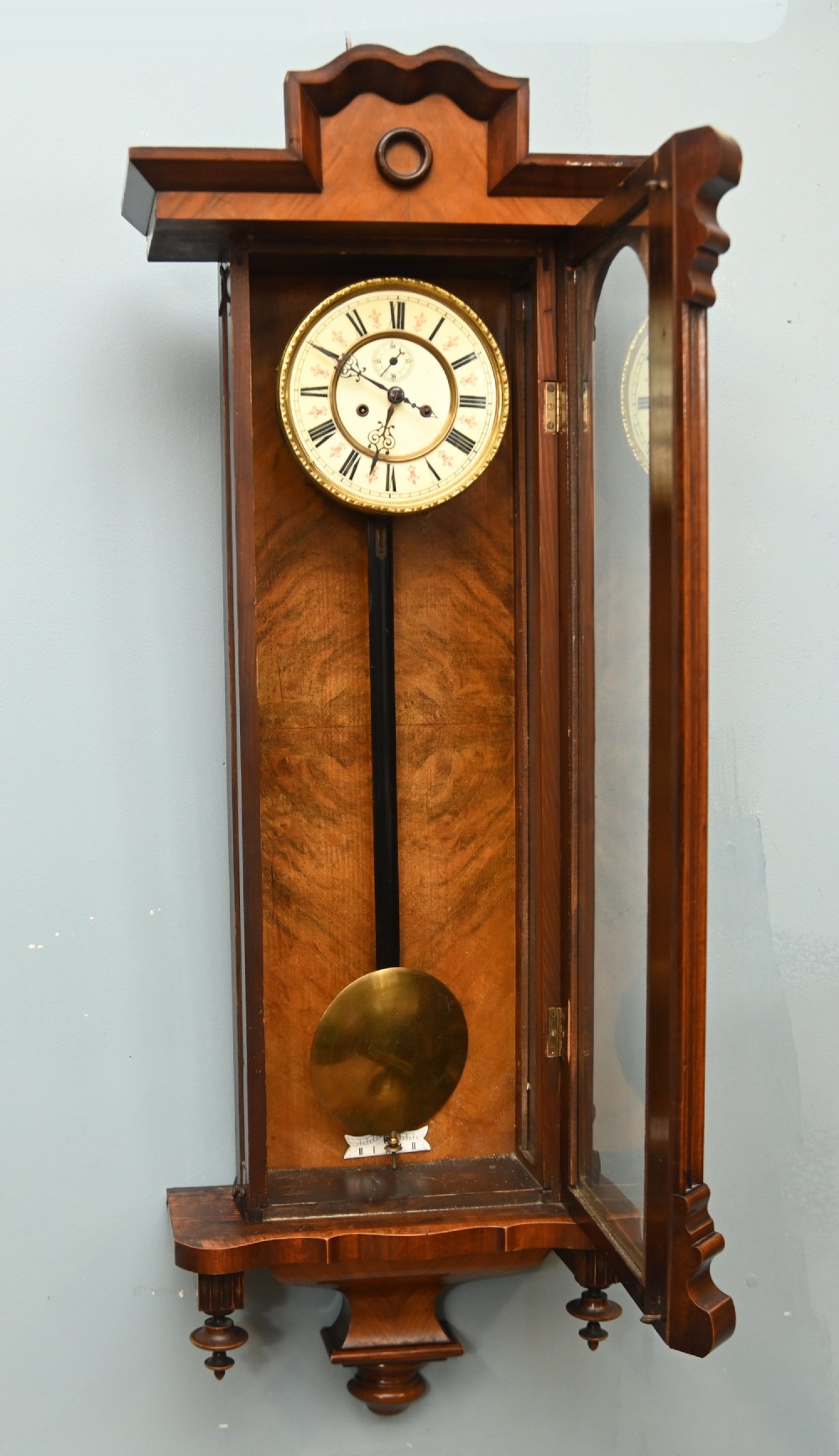 An antique walnut Vienna regulator wall clock featuring a glazed front door, brass pendulum, and turned bottom finials. View VII