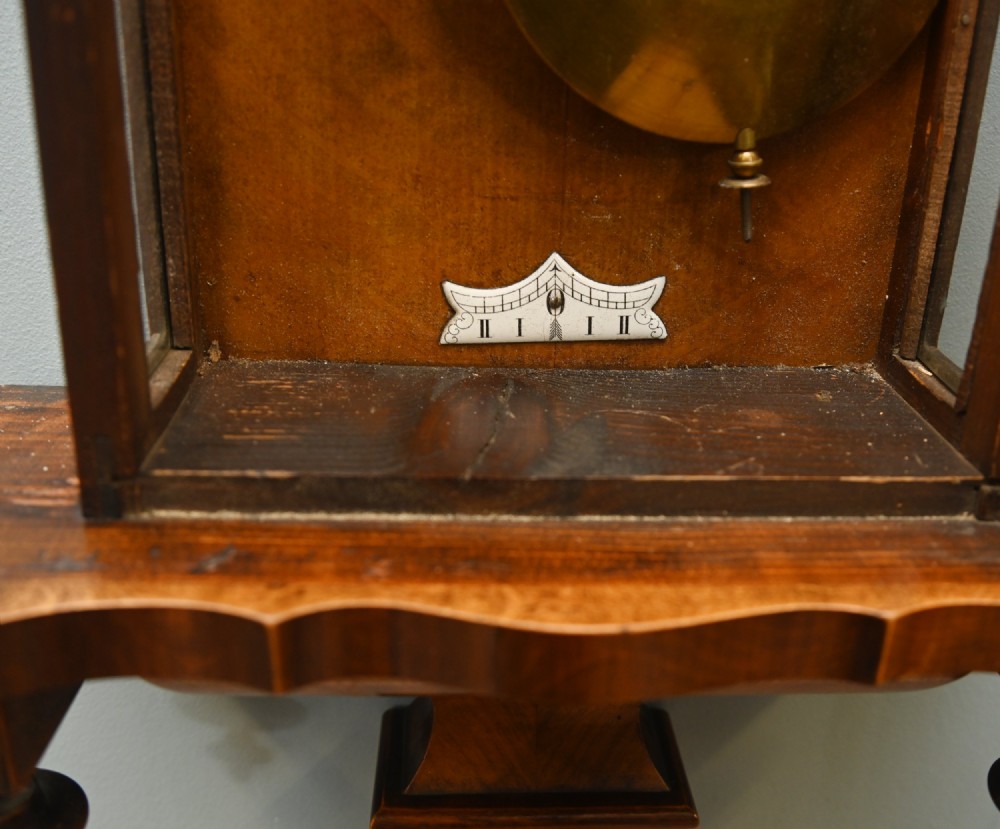 An antique walnut Vienna regulator wall clock featuring a glazed front door, brass pendulum, and turned bottom finials. View VIII