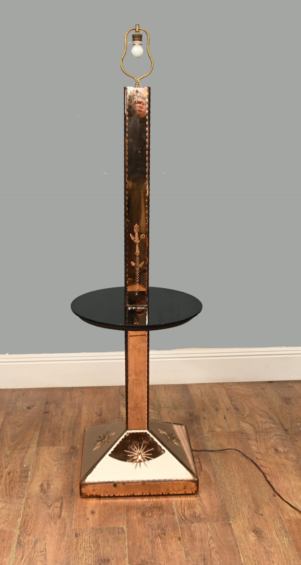 An Art Deco floor lamp featuring peach-tinted mirrored glass panels with etched starburst designs, a central black circular glass cocktail shelf, and a square pyramidal base.