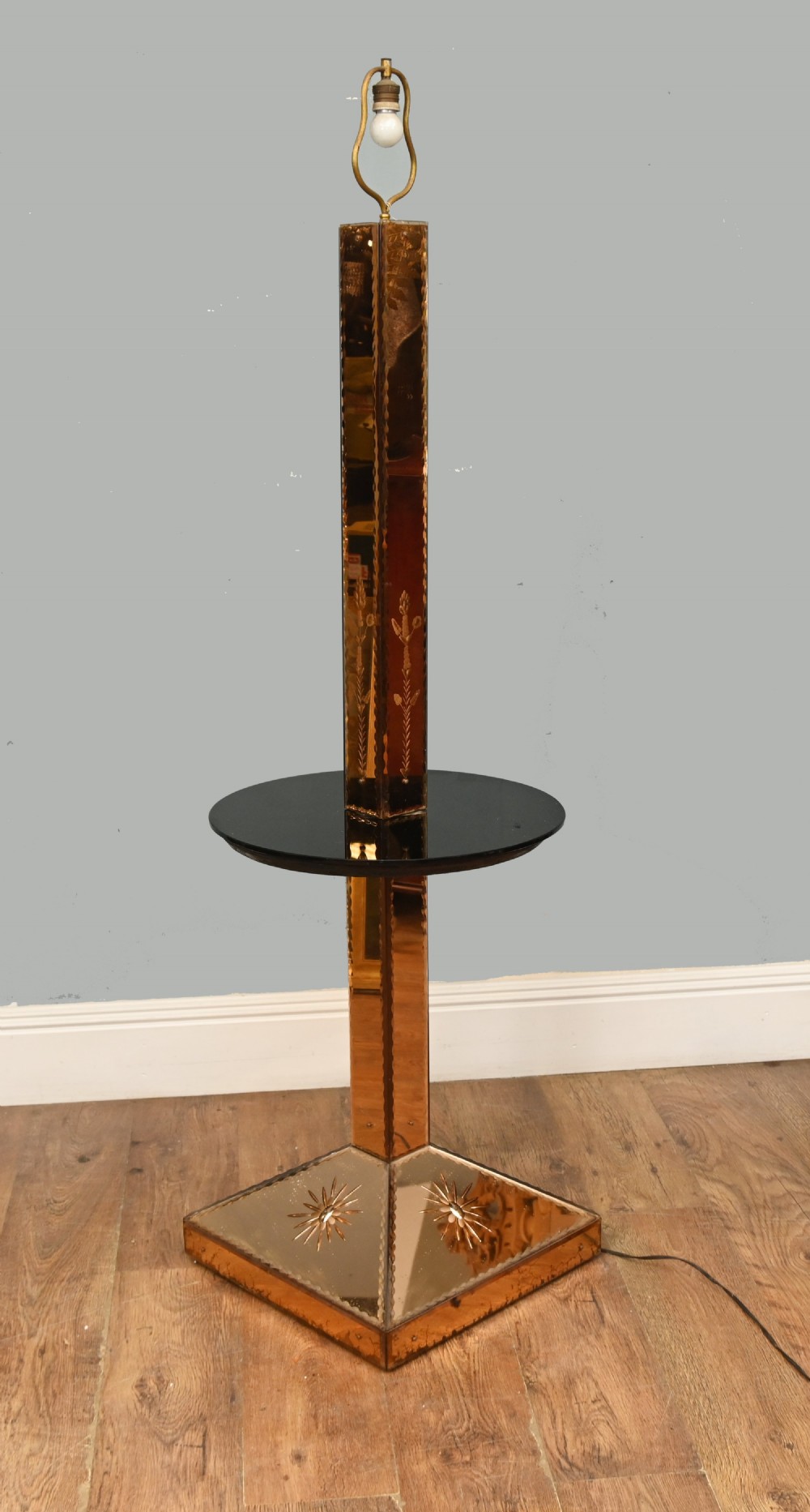An Art Deco floor lamp featuring peach-tinted mirrored glass panels with etched starburst designs, a central black circular glass cocktail shelf, and a square pyramidal base. View VI