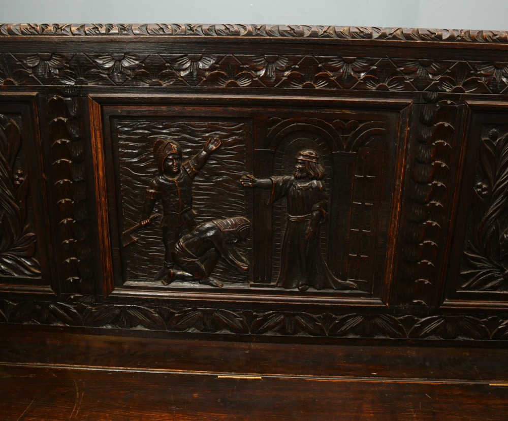 A dark Renaissance Revival carved oak hall settle featuring narrative relief panels on the backrest, carved lion head armrests, and a lifted storage seat. View III