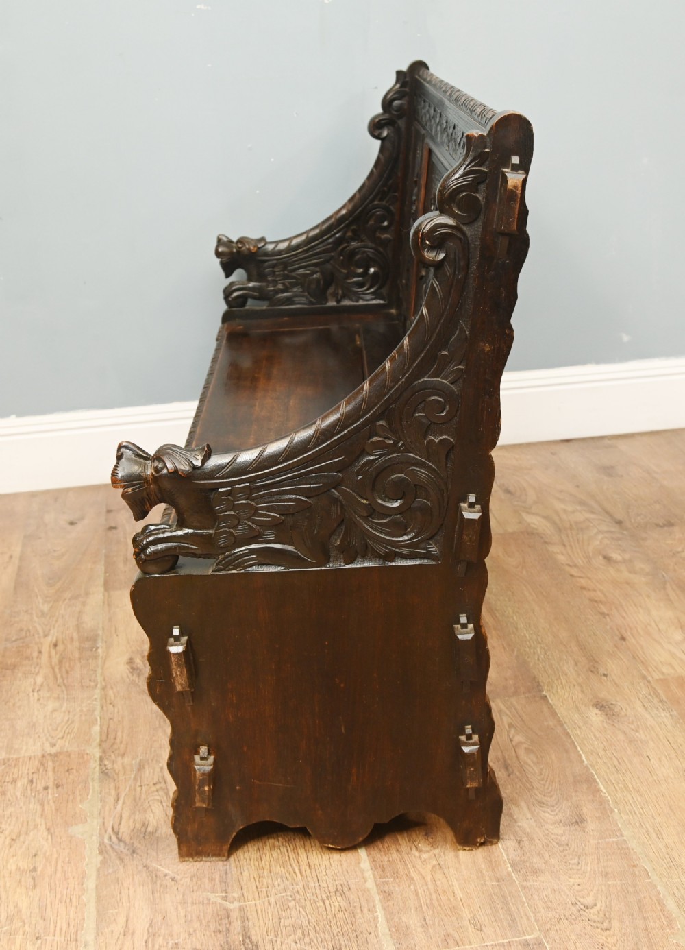 A dark Renaissance Revival carved oak hall settle featuring narrative relief panels on the backrest, carved lion head armrests, and a lifted storage seat. View VII