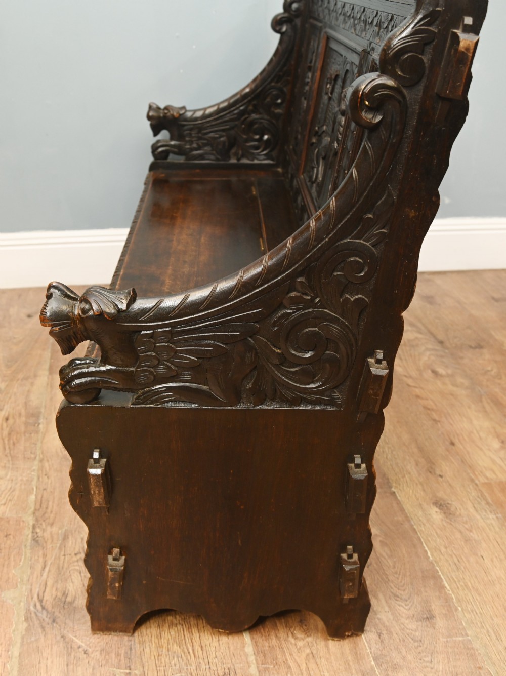 A dark Renaissance Revival carved oak hall settle featuring narrative relief panels on the backrest, carved lion head armrests, and a lifted storage seat. View VIII