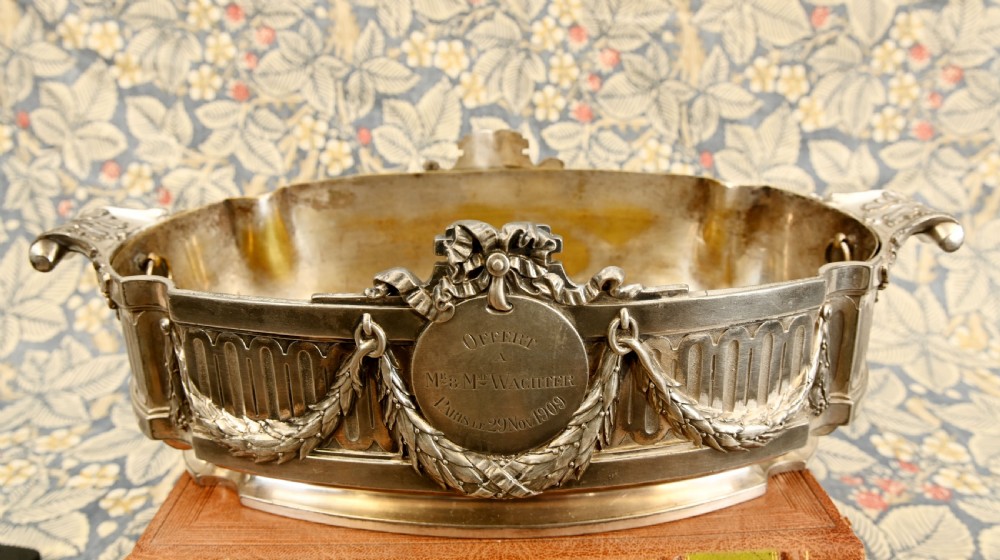 An oval Neoclassical silver-plated jardiniere featuring ribbon bow motifs, hanging laurel swags, twin end handles, and an engraved central medallion dated 1909. View II