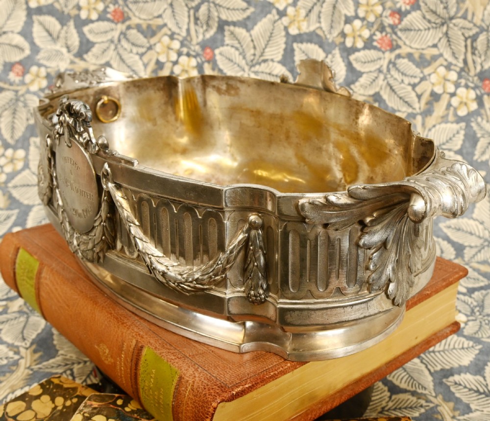 An oval Neoclassical silver-plated jardiniere featuring ribbon bow motifs, hanging laurel swags, twin end handles, and an engraved central medallion dated 1909. View III