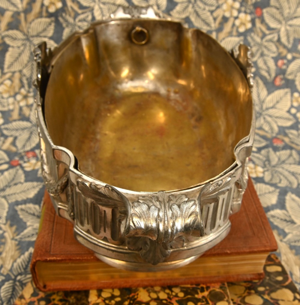 An oval Neoclassical silver-plated jardiniere featuring ribbon bow motifs, hanging laurel swags, twin end handles, and an engraved central medallion dated 1909. View V