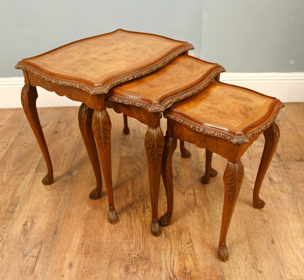 A set of three graduated burr walnut nest tables featuring carved serpentine edges, cabriole legs with carved knees, and claw-and-ball feet.