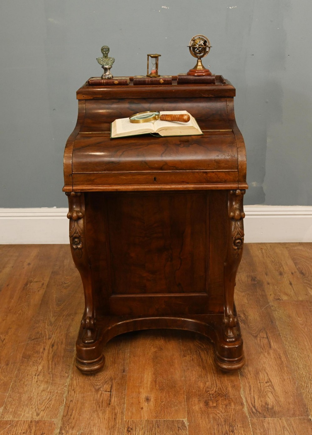 A Victorian walnut Davenport desk featuring a sloped piano-style lid, carved cabriole supports, and a rich wood grain finish.
