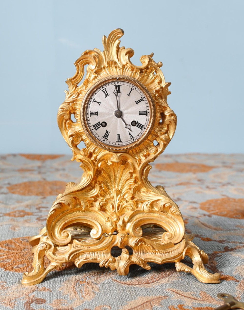 A late 19th-century French Rococo gilt metal mantel clock featuring ornate acanthus leaf scrollwork surrounding a circular dial with Roman numerals.