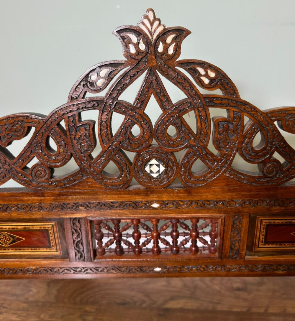A pair of warm brown wooden armchairs featuring elaborate carved openwork crestings and geometric mother-of-pearl inlays across the seats and panels. View III