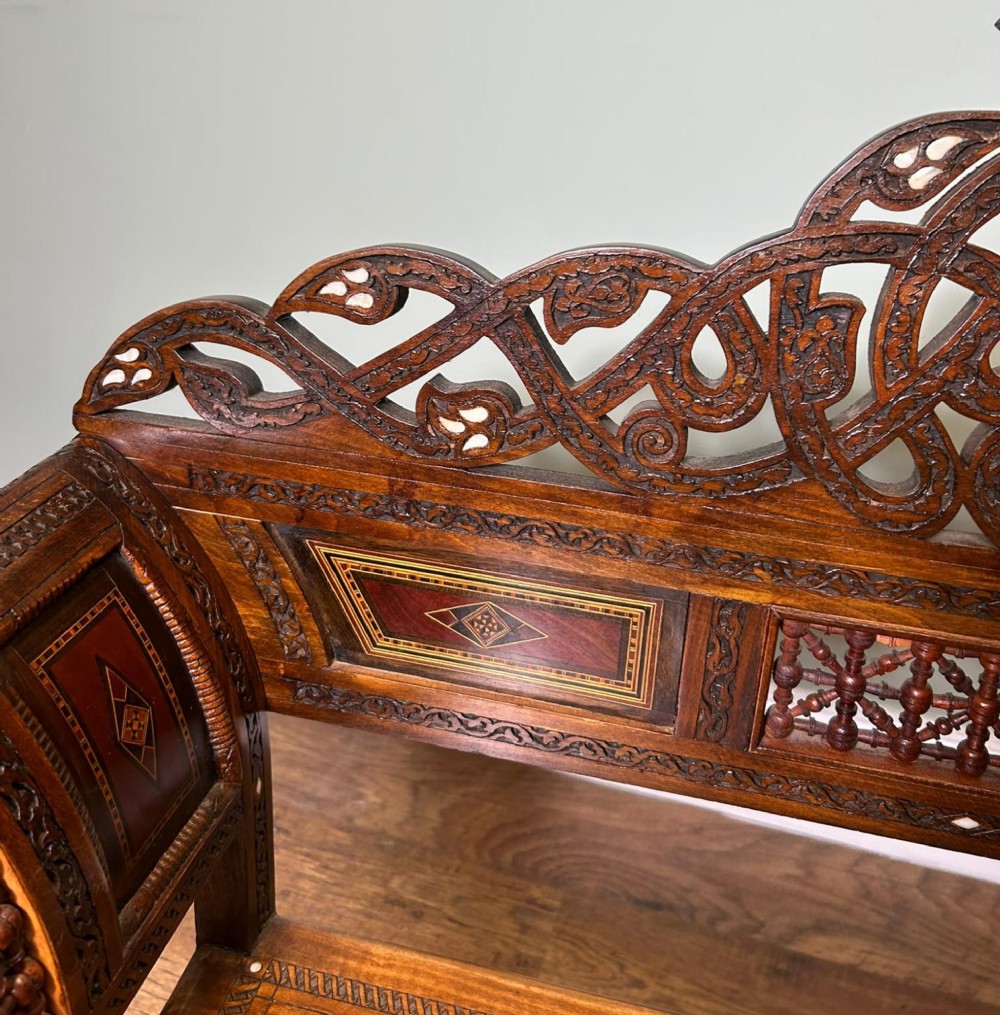 A pair of warm brown wooden armchairs featuring elaborate carved openwork crestings and geometric mother-of-pearl inlays across the seats and panels. View IV