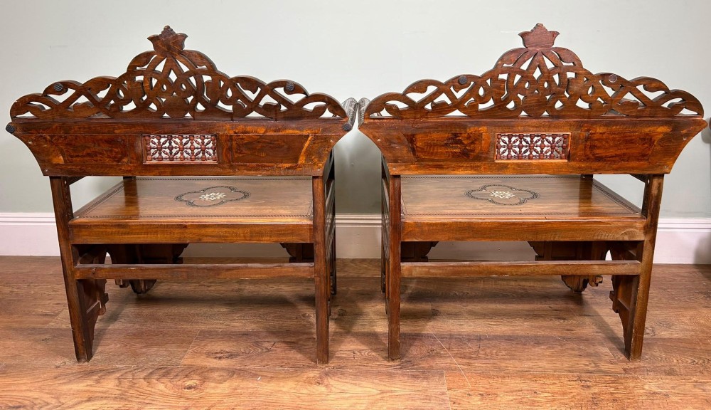 A pair of warm brown wooden armchairs featuring elaborate carved openwork crestings and geometric mother-of-pearl inlays across the seats and panels. View V