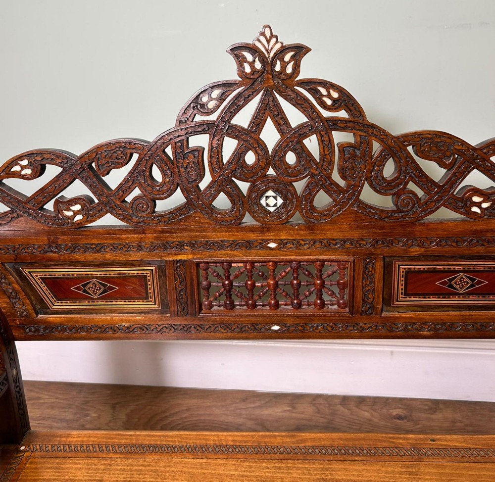 A pair of warm brown wooden armchairs featuring elaborate carved openwork crestings and geometric mother-of-pearl inlays across the seats and panels. View XII