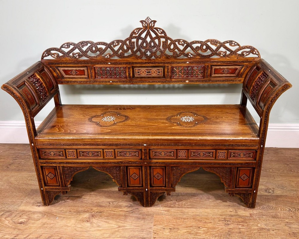 A 19th-century Syrian wooden bench featuring geometric marquetry inlay, mother-of-pearl accents, an openwork carved crest, and arched apron support. View II