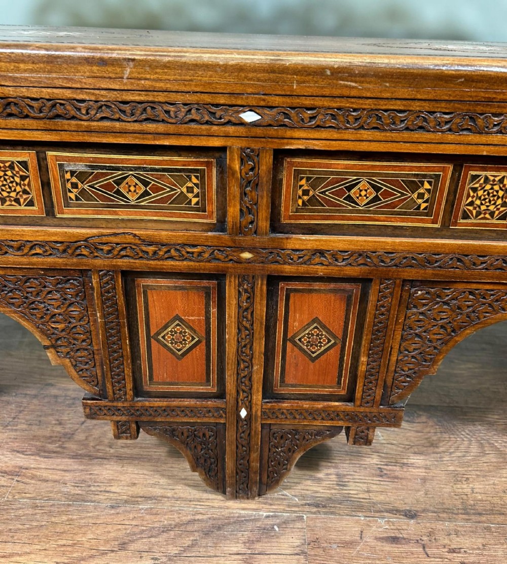 A 19th-century Syrian wooden bench featuring geometric marquetry inlay, mother-of-pearl accents, an openwork carved crest, and arched apron support. View VI