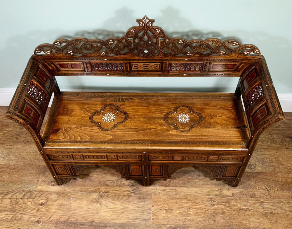 A 19th-century Syrian wooden bench featuring geometric marquetry inlay, mother-of-pearl accents, an openwork carved crest, and arched apron support. View VII
