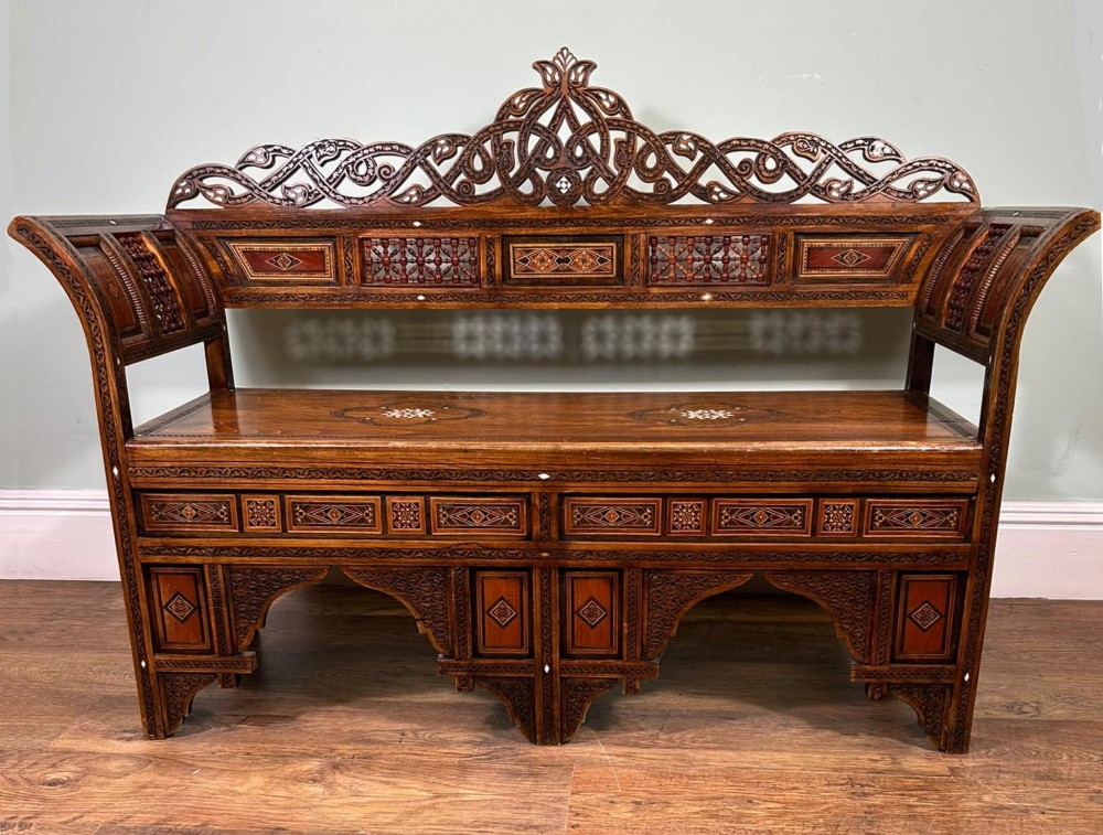A 19th-century Syrian wooden bench featuring geometric marquetry inlay, mother-of-pearl accents, an openwork carved crest, and arched apron support. View VIII