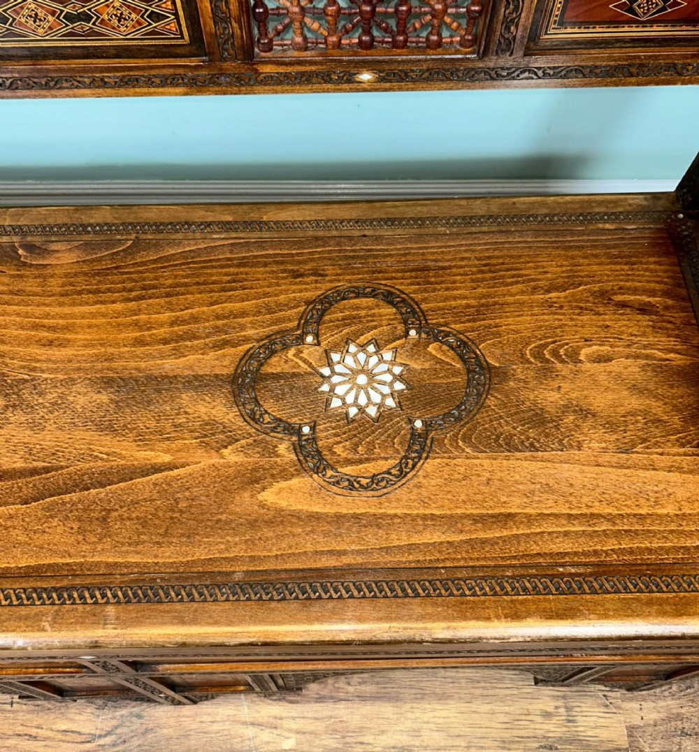 A 19th-century Syrian wooden bench featuring geometric marquetry inlay, mother-of-pearl accents, an openwork carved crest, and arched apron support. View IX