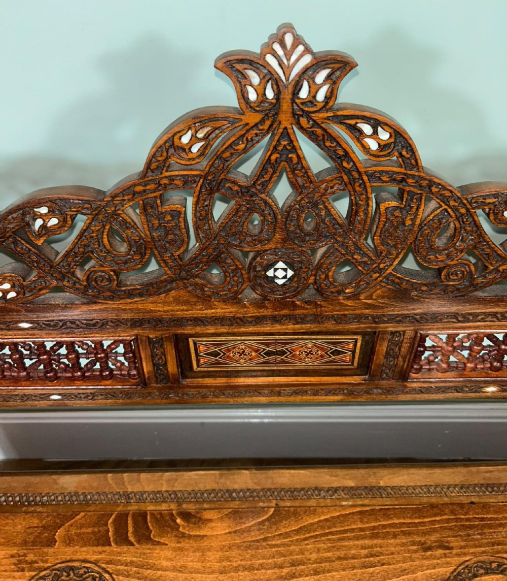 A 19th-century Syrian wooden bench featuring geometric marquetry inlay, mother-of-pearl accents, an openwork carved crest, and arched apron support. View X