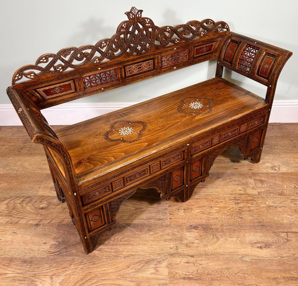 A 19th-century Syrian wooden bench featuring geometric marquetry inlay, mother-of-pearl accents, an openwork carved crest, and arched apron support. View XI