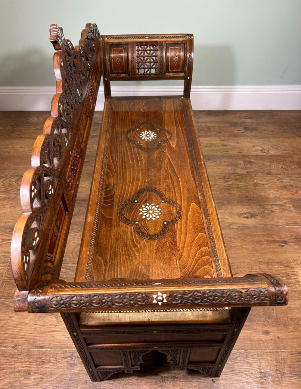 A 19th-century Syrian wooden bench featuring geometric marquetry inlay, mother-of-pearl accents, an openwork carved crest, and arched apron support. View XII