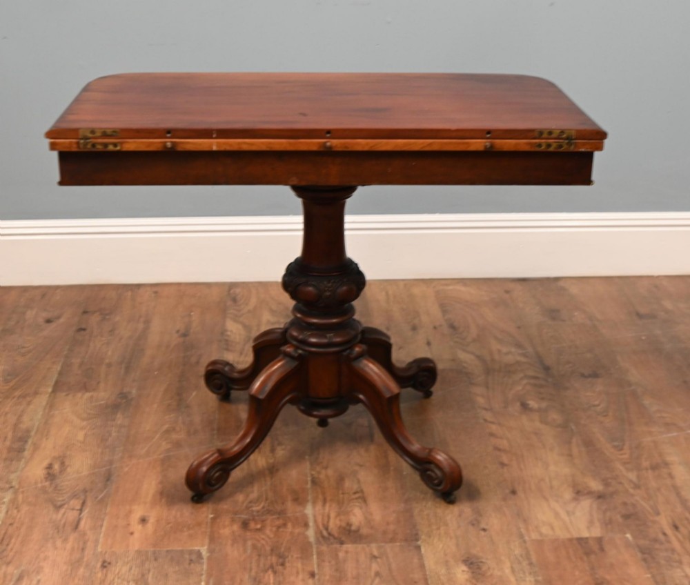 A Victorian mahogany fold-over card table with a rectangular top supported by a central carved pedestal and four scroll-cut legs on castors. View IV