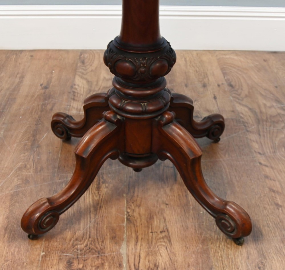 A Victorian mahogany fold-over card table with a rectangular top supported by a central carved pedestal and four scroll-cut legs on castors. View VI