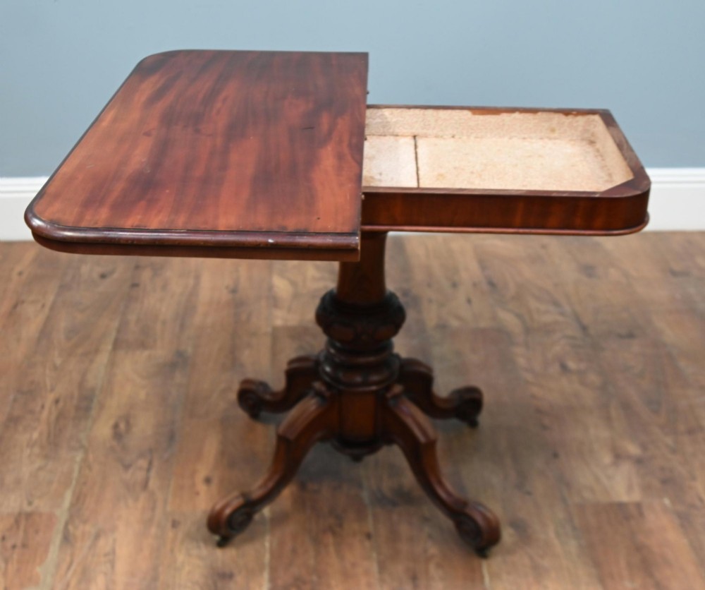 A Victorian mahogany fold-over card table with a rectangular top supported by a central carved pedestal and four scroll-cut legs on castors. View VII