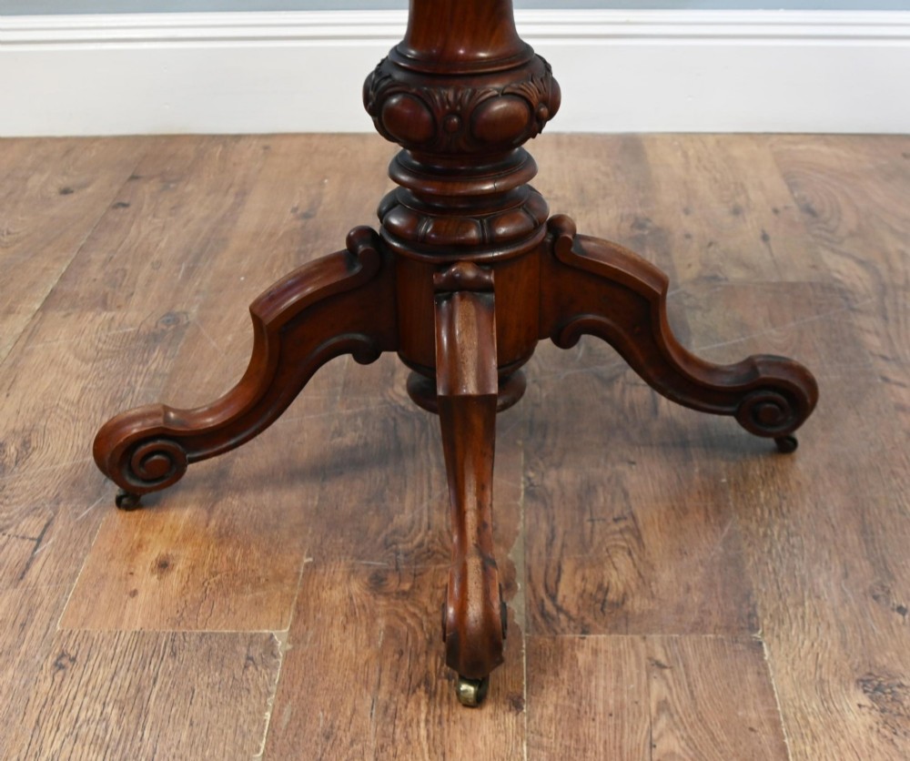 A Victorian mahogany fold-over card table with a rectangular top supported by a central carved pedestal and four scroll-cut legs on castors. View X