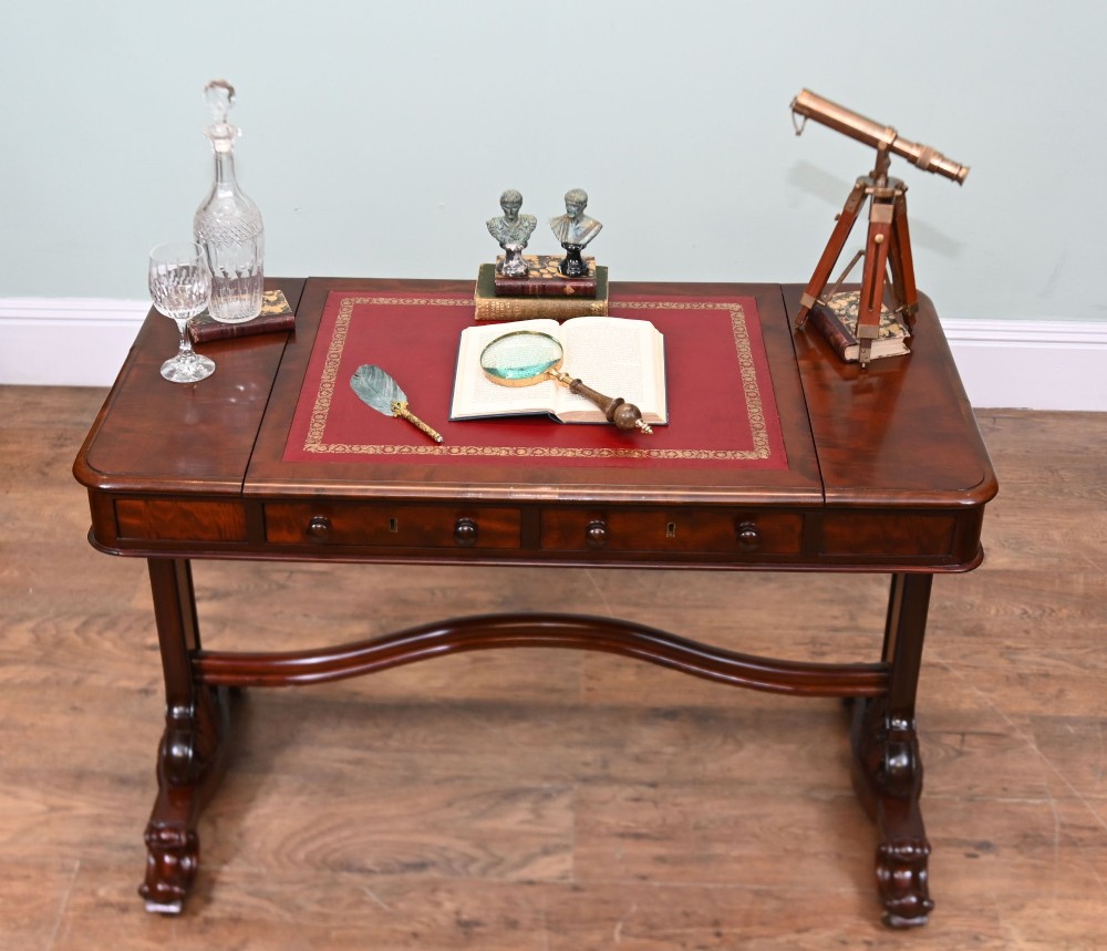 A late Victorian mahogany writing table featuring a central red leather skiver with gold tooling, two frieze drawers, turned end supports, and a curved stretcher. View IV