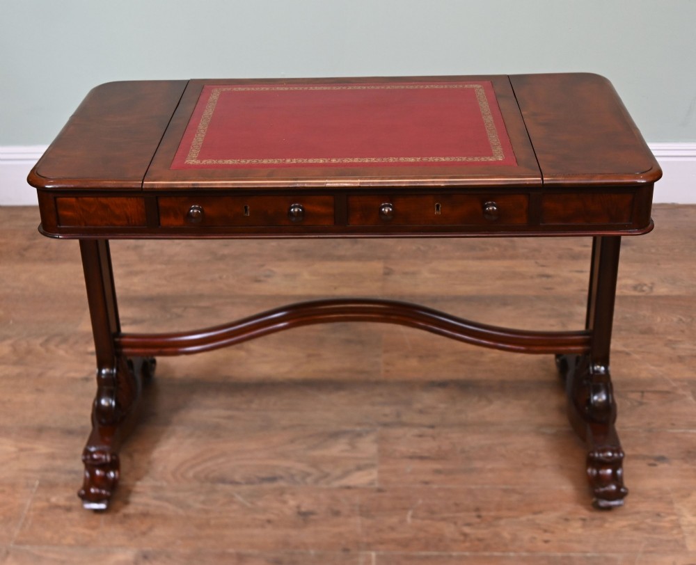 A late Victorian mahogany writing table featuring a central red leather skiver with gold tooling, two frieze drawers, turned end supports, and a curved stretcher. View V