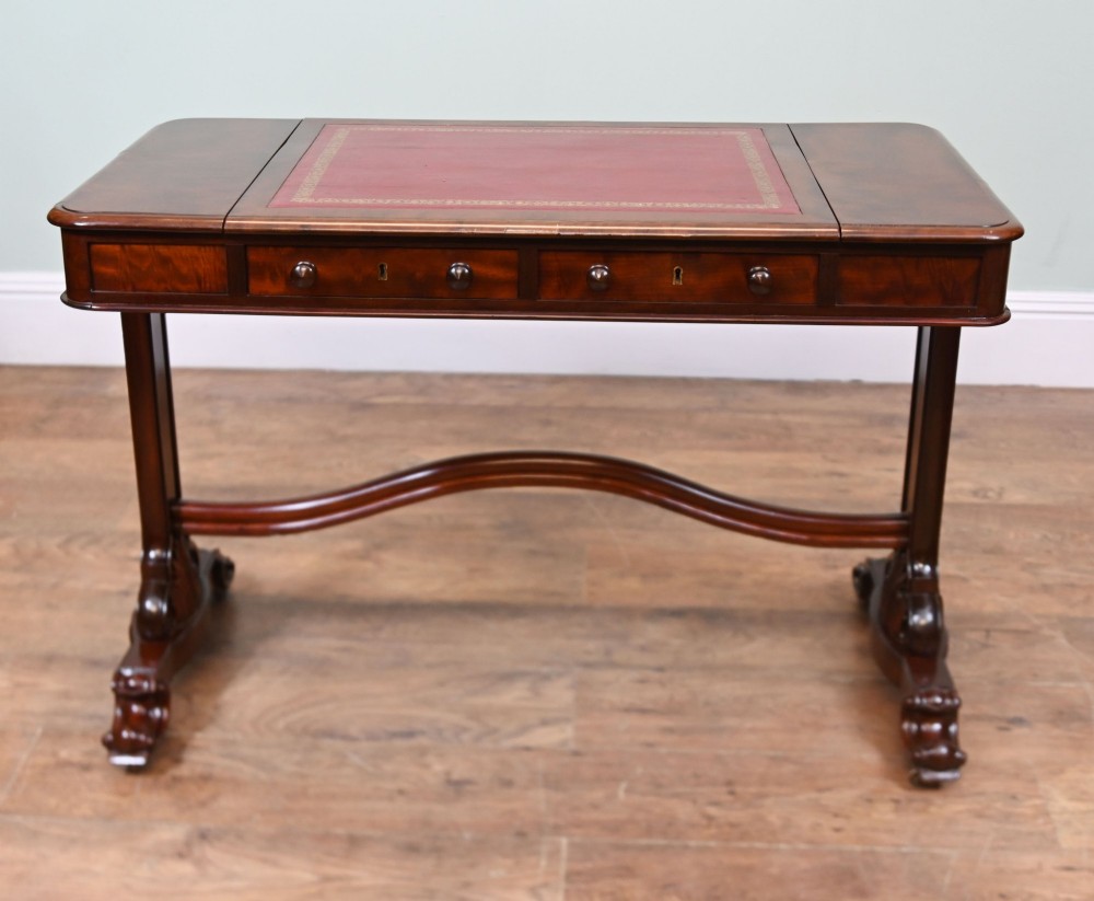 A late Victorian mahogany writing table featuring a central red leather skiver with gold tooling, two frieze drawers, turned end supports, and a curved stretcher.