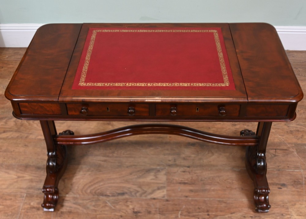 A late Victorian mahogany writing table featuring a central red leather skiver with gold tooling, two frieze drawers, turned end supports, and a curved stretcher. View VI